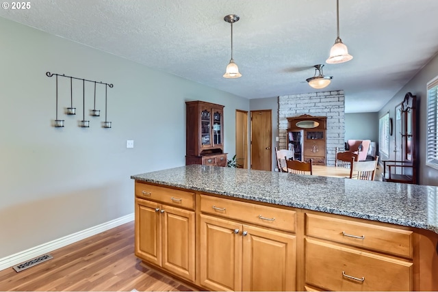 157 NE 11th Dr, Hillsboro, OR 97124 - kitchen with light wood-type flooring, a textured ceiling, baseboards, hanging light fixtures, and stone counters