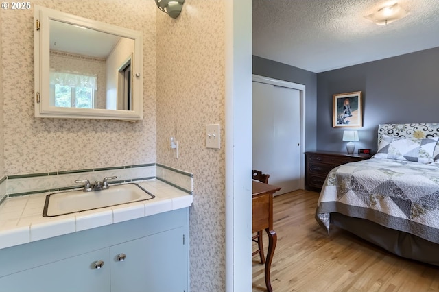 157 NE 11th Dr, Hillsboro, OR 97124 - bedroom with a sink, light wood finished floors, a textured ceiling, wallpapered walls, and a closet