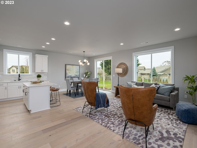 living area with recessed lighting, baseboards, an inviting chandelier, and light wood finished floors