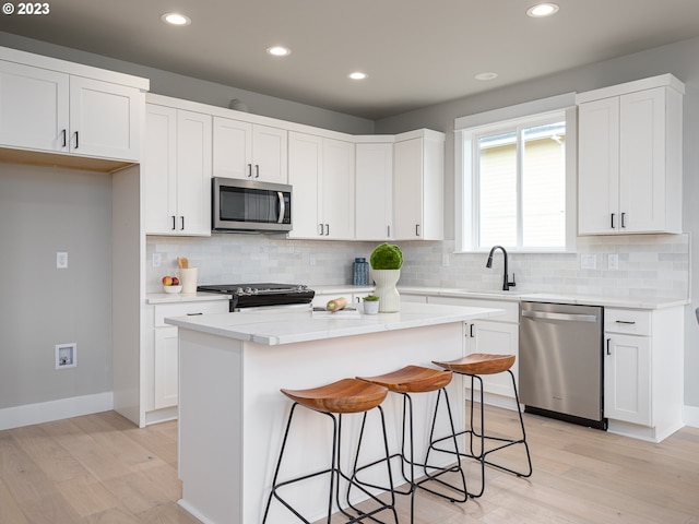 kitchen with a sink, stainless steel appliances, a kitchen island, and white cabinetry