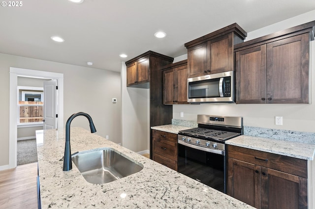 kitchen featuring light wood-style floors, appliances with stainless steel finishes, dark brown cabinetry, and a sink