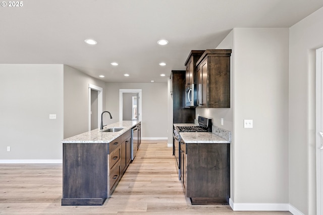 kitchen featuring stainless steel appliances, an island with sink, a sink, and dark brown cabinetry