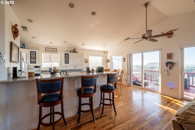 kitchen featuring a breakfast bar area, white cabinetry, light hardwood / wood-style floors, vaulted ceiling, and kitchen peninsula