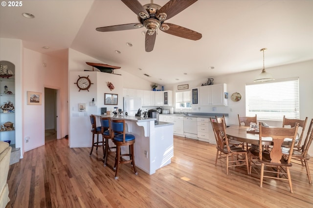 kitchen with white cabinetry, vaulted ceiling, hanging light fixtures, light hardwood / wood-style flooring, and white appliances