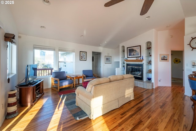 living room with lofted ceiling, built in features, hardwood / wood-style flooring, ceiling fan, and a fireplace