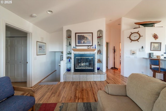 living room featuring a fireplace, vaulted ceiling, built in features, and light hardwood / wood-style flooring