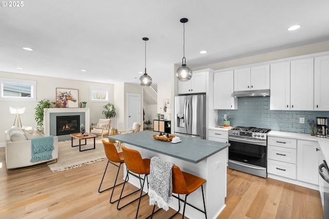 kitchen featuring a kitchen bar, under cabinet range hood, white cabinetry, appliances with stainless steel finishes, and light wood finished floors