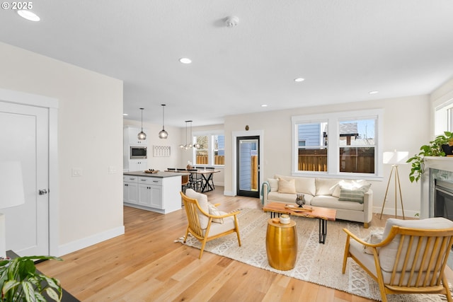 living area with a glass covered fireplace, recessed lighting, baseboards, and light wood finished floors