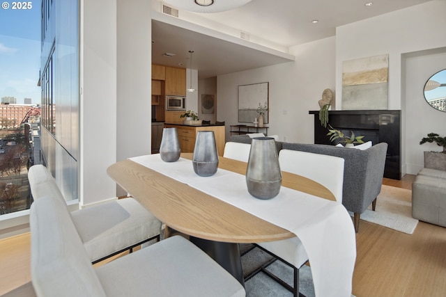 dining room featuring a glass covered fireplace, visible vents, and light wood-style flooring