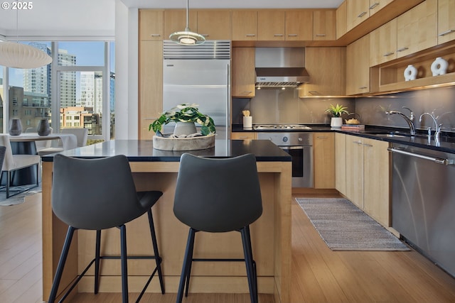 kitchen featuring dark countertops, decorative backsplash, appliances with stainless steel finishes, wall chimney exhaust hood, and a sink