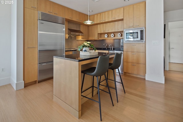 kitchen with a kitchen island, built in appliances, dark countertops, modern cabinets, and light wood-type flooring