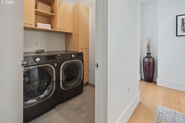 washroom with baseboards, cabinet space, light wood-style flooring, and washing machine and clothes dryer