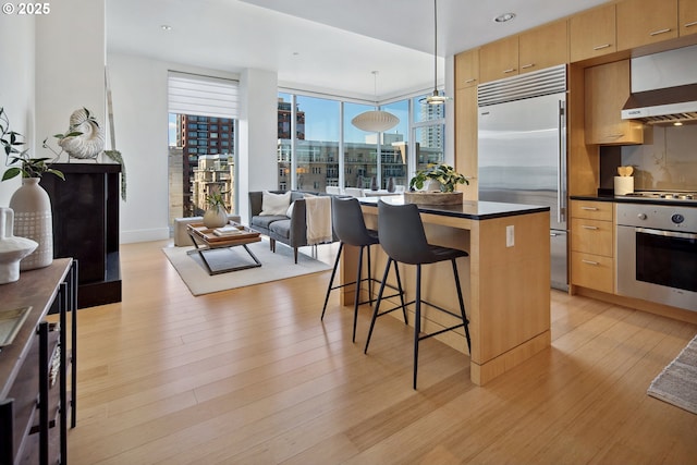 kitchen featuring a kitchen island, stainless steel appliances, a kitchen bar, dark countertops, and light wood-type flooring