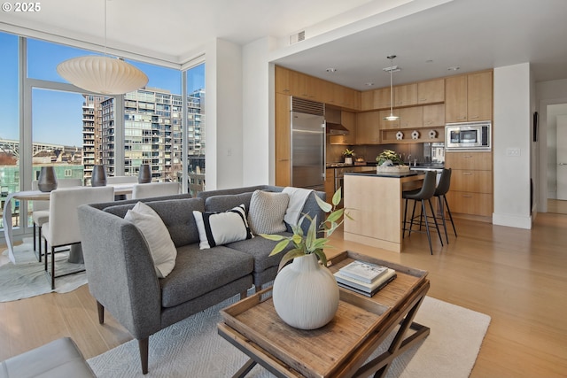 living area with light wood finished floors, visible vents, a view of city, and expansive windows