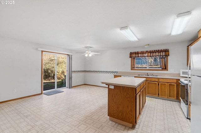 kitchen with brown cabinets, light countertops, a kitchen island, a sink, and white appliances