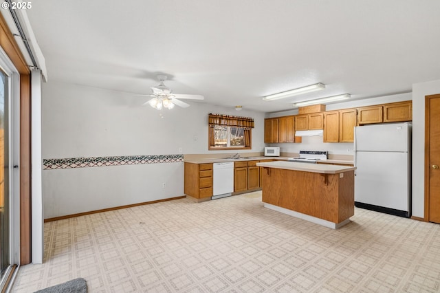 kitchen featuring light countertops, a kitchen island, a sink, white appliances, and under cabinet range hood