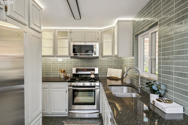 7335 SE 48th Ave, Portland, OR 97206 - kitchen featuring appliances with stainless steel finishes, a sink, tasteful backsplash, dark stone countertops, and glass insert cabinets