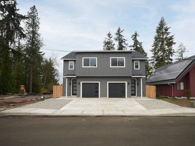 contemporary house featuring an attached garage, board and batten siding, driveway, and fence