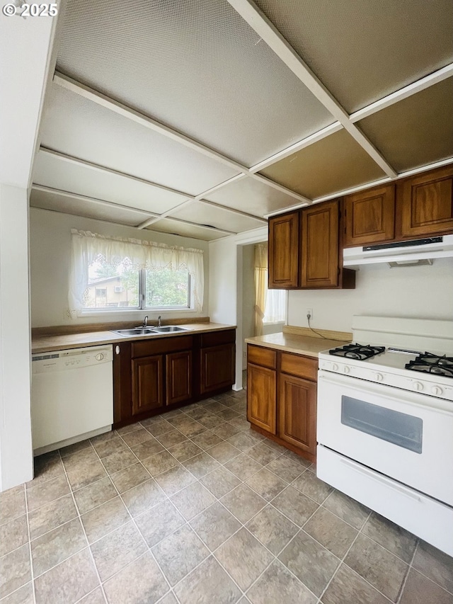 kitchen with white appliances, brown cabinetry, a sink, light countertops, and under cabinet range hood