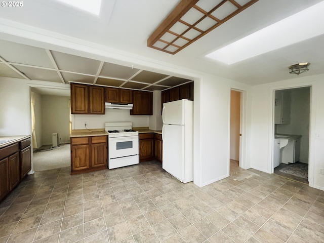 kitchen featuring white appliances, light countertops, baseboards, and under cabinet range hood