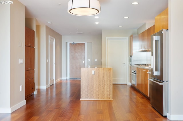 kitchen featuring hardwood / wood-style floors, stainless steel appliances, a kitchen island, and light stone countertops