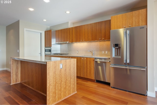 kitchen featuring light wood-type flooring, stainless steel appliances, light stone countertops, sink, and tasteful backsplash