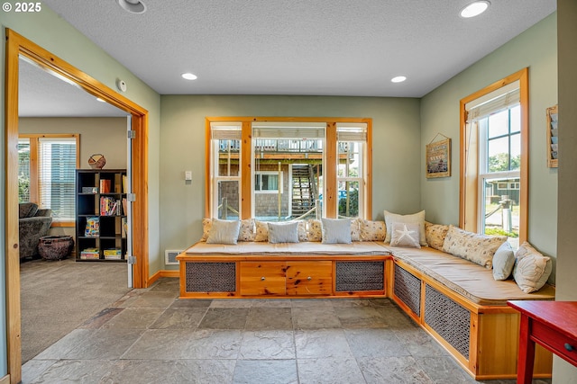sitting room featuring a textured ceiling, visible vents, baseboards, recessed lighting, and stone tile floors