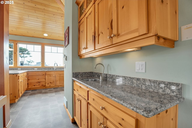 kitchen featuring wood ceiling, stone countertops, glass insert cabinets, and a sink