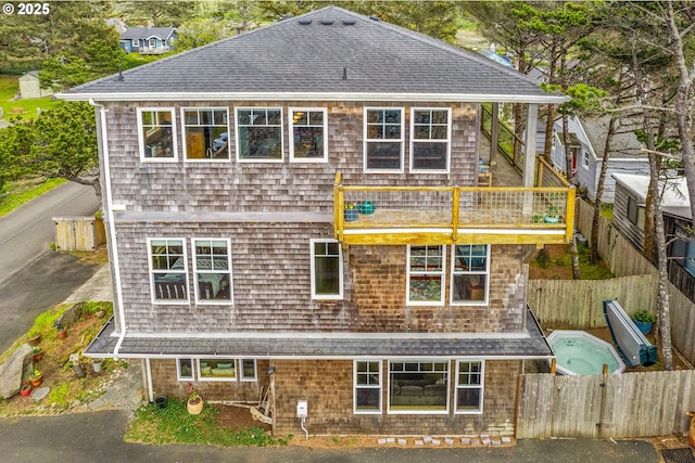rear view of property with a fenced backyard, roof with shingles, and a balcony