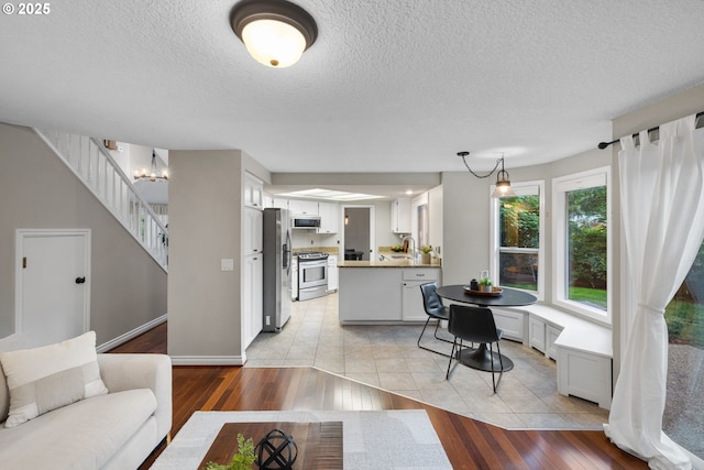 15421 SW Thurston Ln, Portland, OR 97224 - living area featuring light wood-style flooring, a textured ceiling, stairway, baseboards, and a chandelier