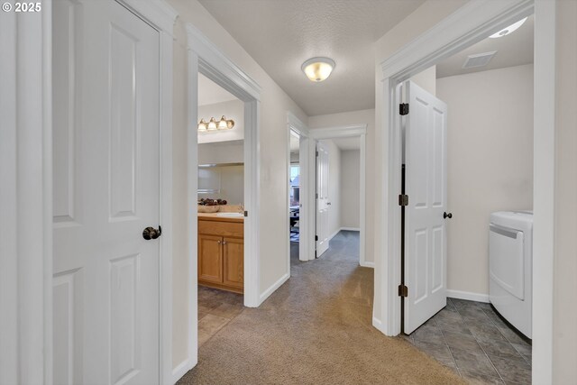 hall with carpet floors, a sink, visible vents, baseboards, and washer / dryer