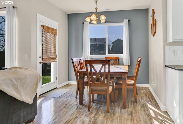 dining room featuring light wood-type flooring, baseboards, visible vents, and a chandelier