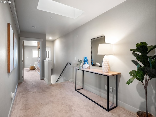 hallway featuring carpet floors, a skylight, baseboards, and an upstairs landing