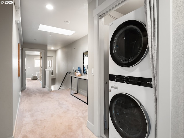 washroom with a skylight, laundry area, baseboards, stacked washer / dryer, and carpet floors