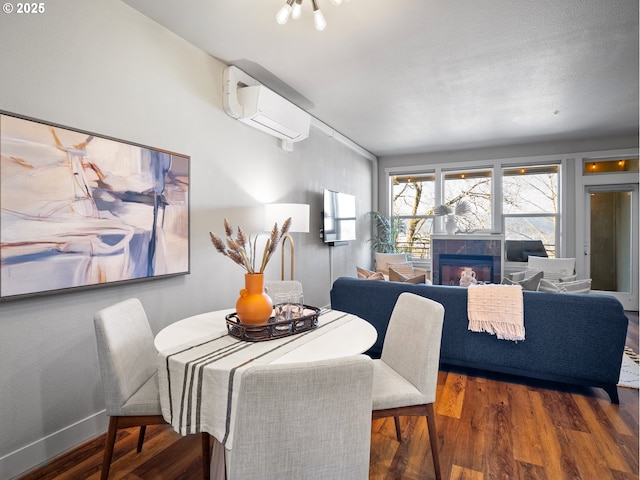 dining room featuring a wall unit AC, baseboards, wood finished floors, and a glass covered fireplace