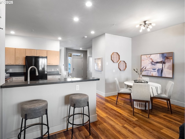 kitchen with a breakfast bar, dark countertops, recessed lighting, dark wood-type flooring, and black fridge