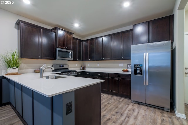 kitchen with appliances with stainless steel finishes, sink, dark brown cabinetry, kitchen peninsula, and light hardwood / wood-style flooring