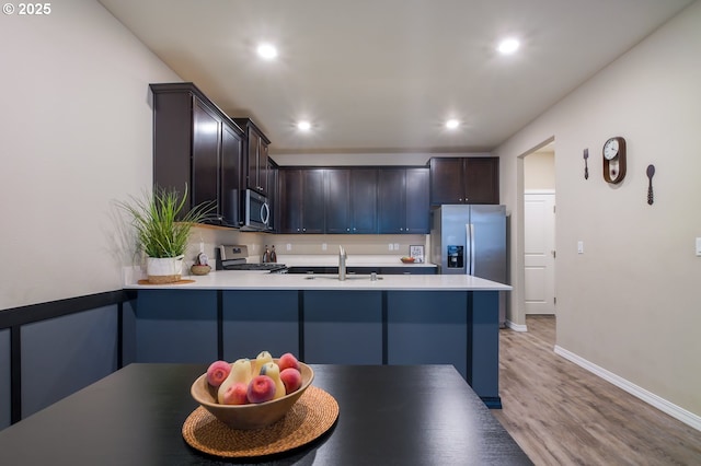 kitchen with sink, kitchen peninsula, stainless steel appliances, dark brown cabinets, and light wood-type flooring