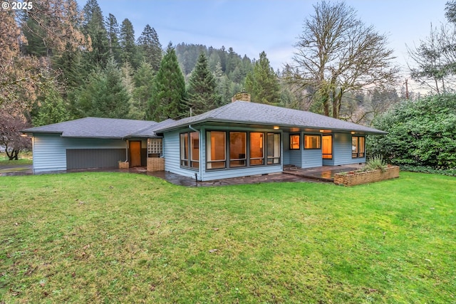 rear view of property with a lawn, a wooded view, a chimney, and covered porch