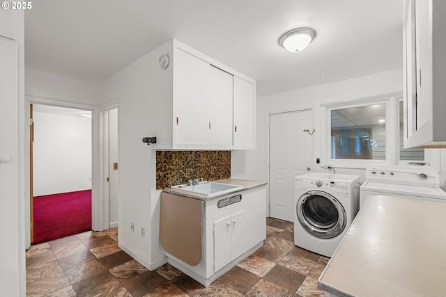 laundry area with stone finish floor, washing machine and clothes dryer, cabinet space, a sink, and baseboards