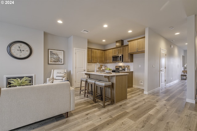 kitchen featuring appliances with stainless steel finishes, an island with sink, sink, a kitchen bar, and light hardwood / wood-style floors