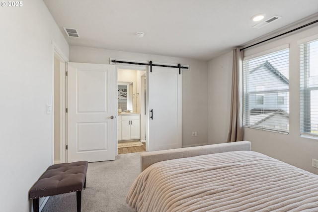 carpeted bedroom featuring a barn door, ensuite bath, and visible vents