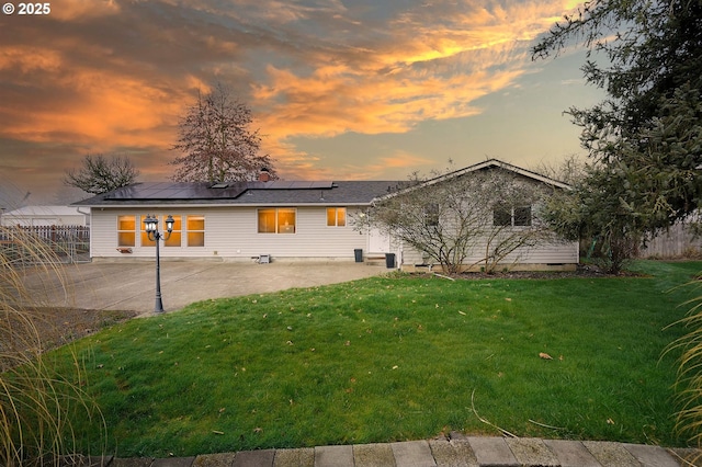 back of property at dusk featuring a patio area, solar panels, a yard, and fence