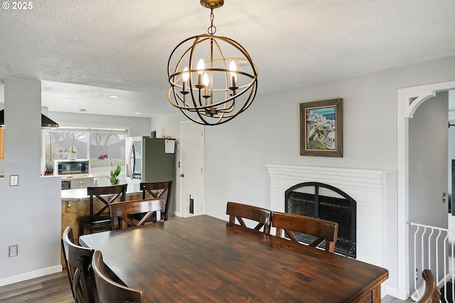 dining room with a brick fireplace, a chandelier, wood finished floors, arched walkways, and a textured ceiling