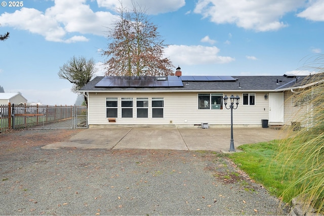 rear view of house with a gate, a patio area, fence, and roof mounted solar panels