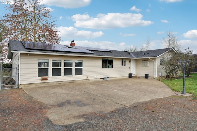 rear view of property with solar panels, a patio, a gate, and a chimney