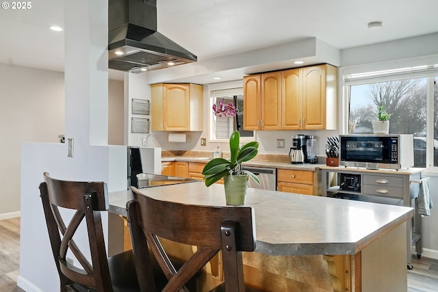 kitchen with light brown cabinets, light wood finished floors, stainless steel appliances, light countertops, and wall chimney exhaust hood