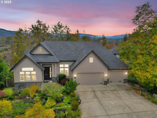 view of front of home featuring an attached garage, a shingled roof, concrete driveway, stone siding, and a mountain view