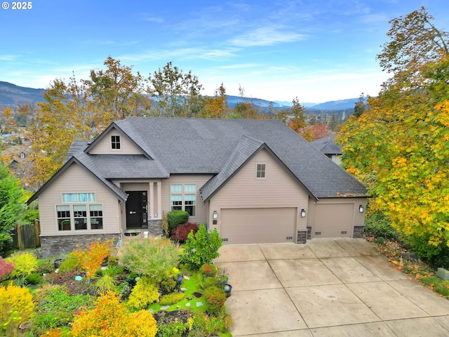 view of front of property featuring driveway, stone siding, a mountain view, a shingled roof, and a garage