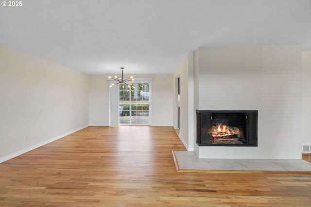 unfurnished living room featuring visible vents, light wood-style flooring, a multi sided fireplace, a chandelier, and baseboards